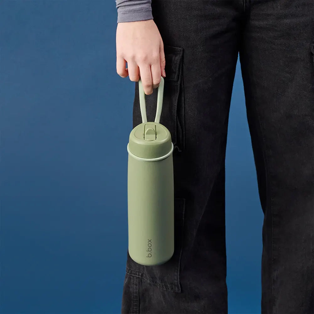 Main tenant par sa poignée la gourde isotherme b.box 690 ml Olive vert olive, sur fond bleu